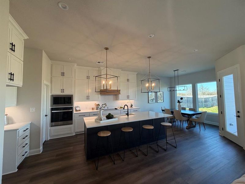 Kitchen with a kitchen breakfast bar, stainless steel appliances, a center island with sink, dark wood-type flooring, and suspended lighting
