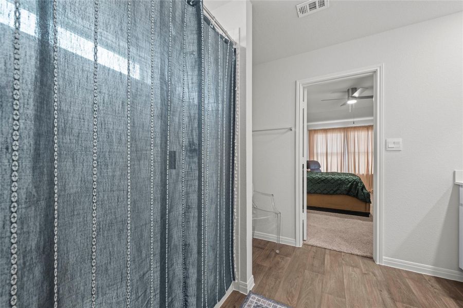 Hardwood-style flooring extends from the bathroom into the adjoining bedroom, offering a harmonious transition.