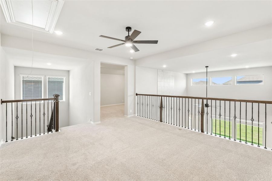 Open upstairs loft with carpet, ceiling fan, and wrought iron stair railing along open balcony