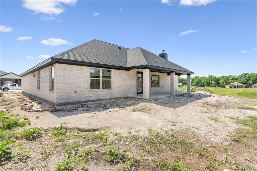 Rear view of property with a shingled roof, brick siding, a chimney, and a patio Rear view of property with a shingled roof, brick siding, a chimney, and a patio