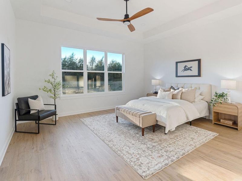 Bedroom with a tray ceiling, ceiling fan, and light wood-type flooring