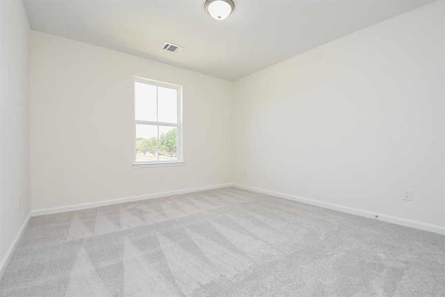 An empty room with beige walls, a window, and gray carpet flooring.