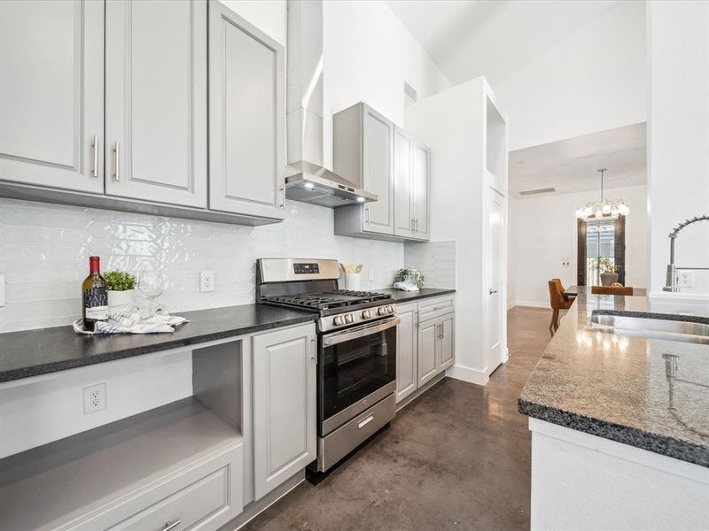 Kitchen featuring wall chimney range hood, sink, stainless steel range with gas stovetop, white cabinetry, and hanging light fixtures