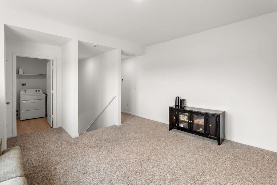 View of upstairs family room with staircase in the background, utility room to the left, primary bedroom to the right View of upstairs family room with staircase in the background, utility room to the left, primary bedroom to the right