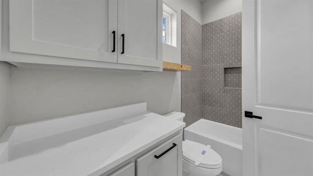 Bathroom featuring a white bathtub with a tiled surround, an integrated shower niche, and a window