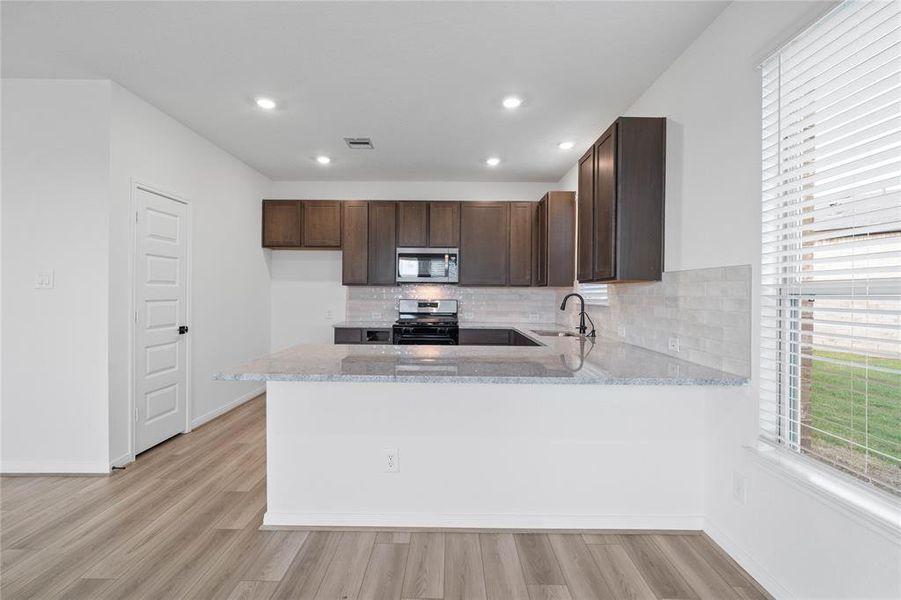 This spacious kitchen features high ceilings, stained wood cabinets, granite countertops, SS appliances, modern tile backsplash, recessed lighting, extended countertop for breakfast bar, and pantry all overlooking your huge family room.