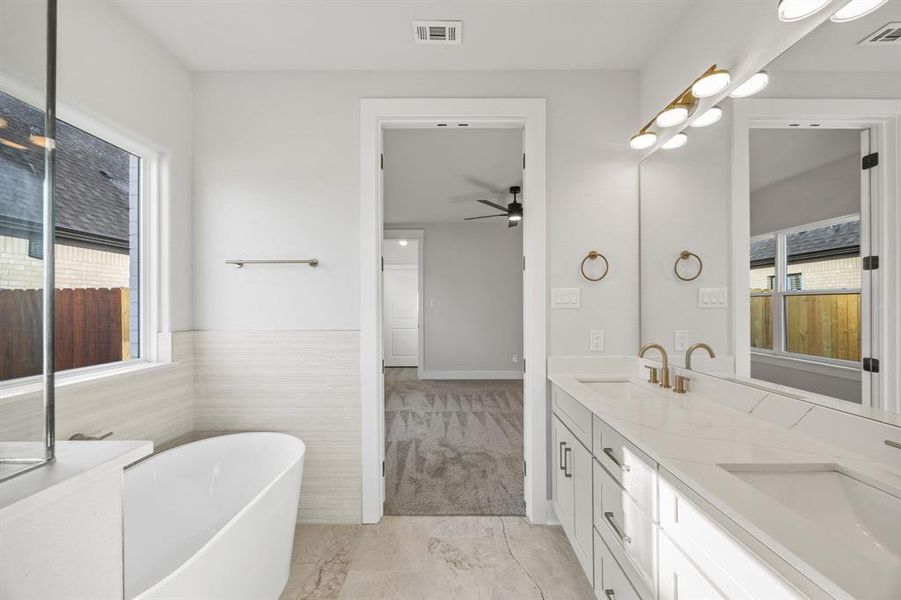Full bath featuring double vanity, a freestanding bath, a ceiling fan, and light marble finish floors