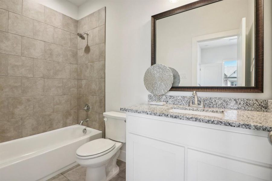 Full bathroom with tile patterned floors, tiled shower / bath combo, toilet, and vanity