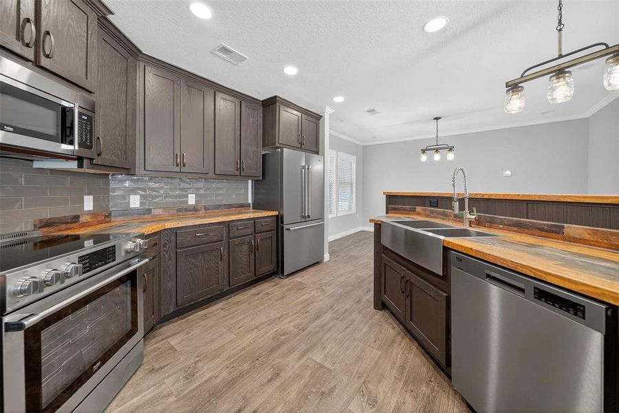 Kitchen with butcher block counters, appliances with stainless steel finishes, dark brown cabinets, decorative light fixtures, and light wood finished floors Kitchen with butcher block counters, appliances with stainless steel finishes, dark brown cabinets, decorative light fixtures, and light wood finished floors
