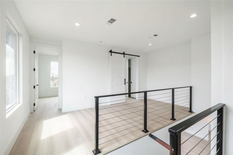 Hall featuring a barn door, light wood-style flooring, and recessed lighting