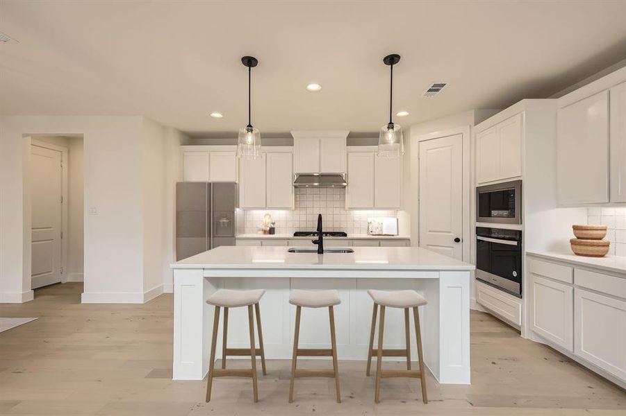 Virtually staged photo - Kitchen with appliances with stainless steel finishes, light countertops, a center island with sink, light wood finished floors, and recessed lighting Virtually staged photo - Kitchen with appliances with stainless steel finishes, light countertops, a center island with sink, light wood finished floors, and recessed lighting