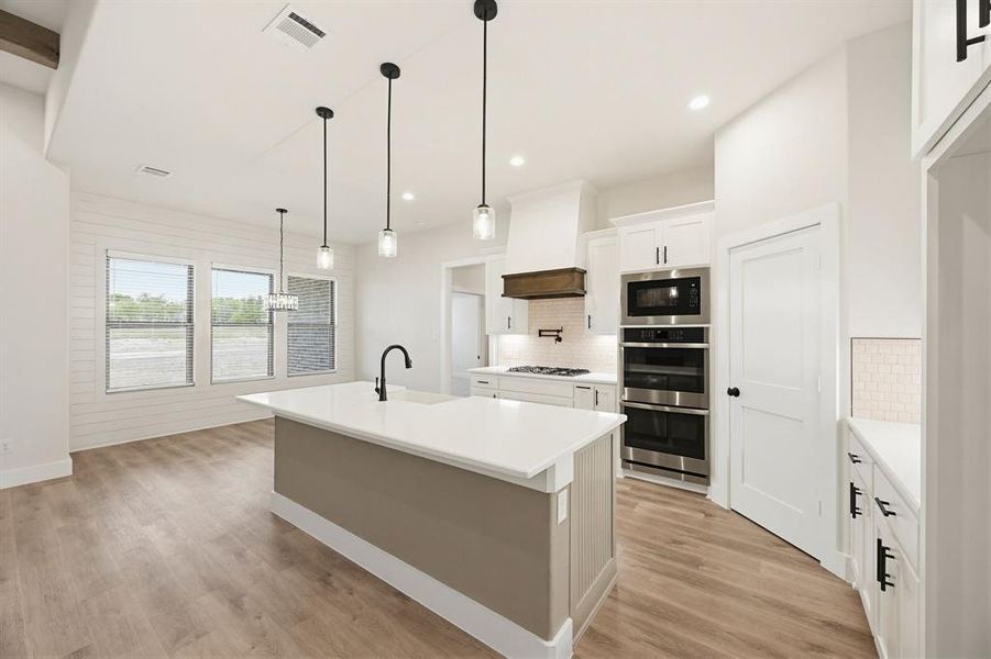 Open-concept kitchen featuring a large island with a gooseneck faucet, light wood-finish flooring, white cabinetry, stainless steel appliances, and recessed lighting