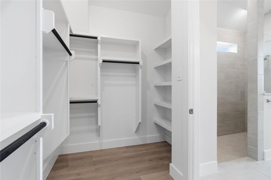 The spacious walk-in closet is equipped with clean white shelving and sturdy matte black hanging rods, offering extensive solutions for organizing an entire wardrobe.