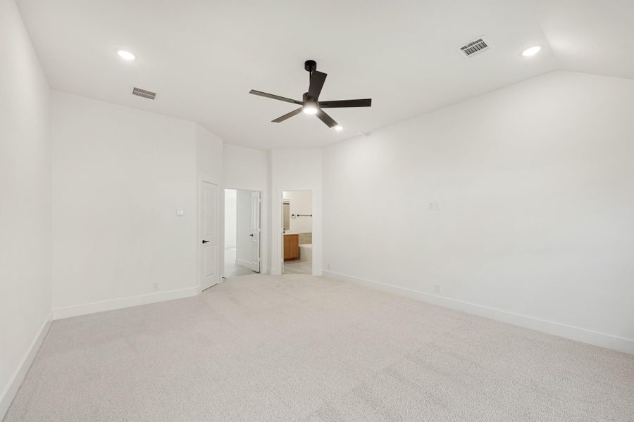 Spacious empty bedroom with carpet, ceiling fan, and open doorway to ensuite bathroom