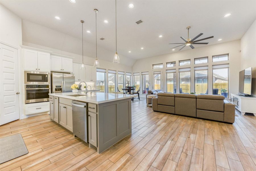 Kitchen with hanging light fixtures, stainless steel appliances, open floor plan, a kitchen island with sink, and light wood-type flooring
