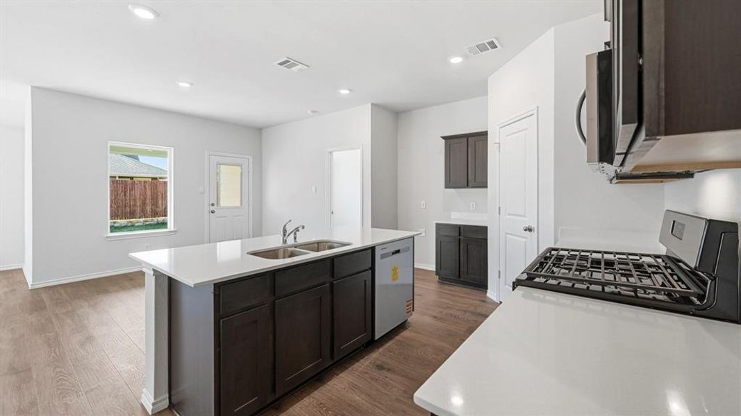 Kitchen with stainless steel appliances, a kitchen island with sink, dark wood-style flooring, light stone counters, and recessed lighting Kitchen with stainless steel appliances, a kitchen island with sink, dark wood-style flooring, light stone counters, and recessed lighting