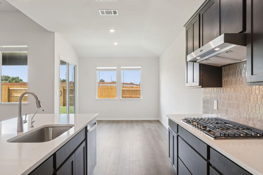 Kitchen featuring light wood finished floors, light stone countertops, appliances with stainless steel finishes, range hood, and backsplash Kitchen featuring light wood finished floors, light stone countertops, appliances with stainless steel finishes, range hood, and backsplash