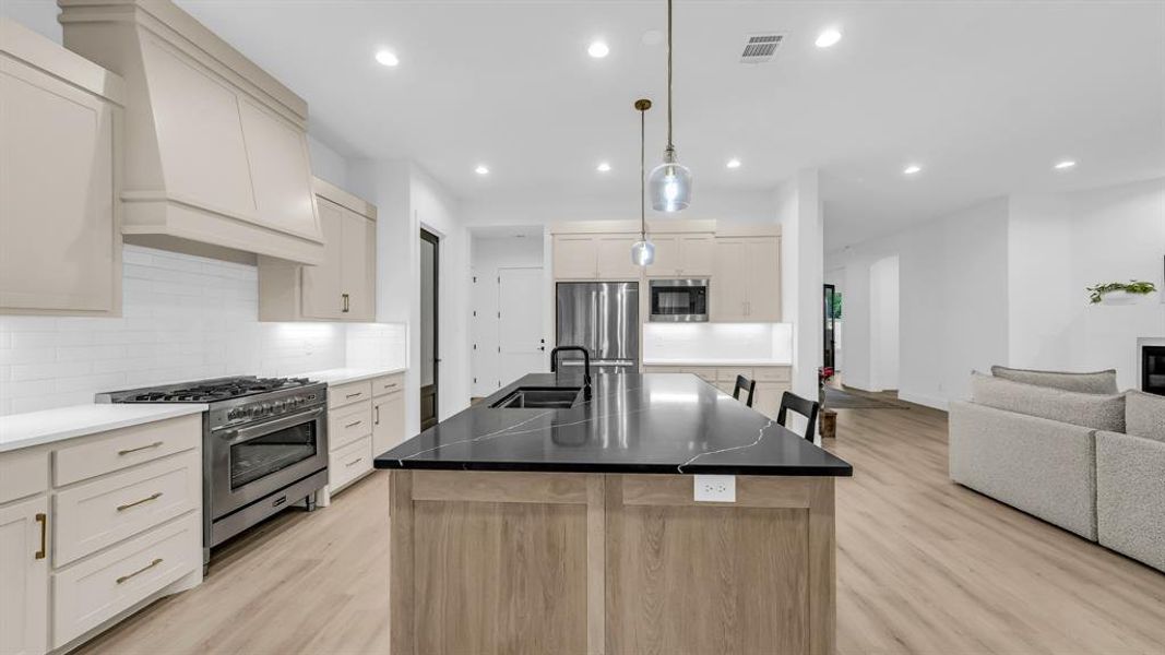 Kitchen with appliances with stainless steel finishes, a sink, light wood-style floors, open floor plan, and tasteful backsplash Kitchen with appliances with stainless steel finishes, a sink, light wood-style floors, open floor plan, and tasteful backsplash