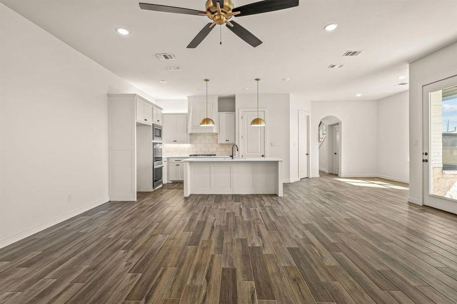 Unfurnished living room featuring arched walkways, dark wood-style floors, ceiling fan, recessed lighting, and baseboards