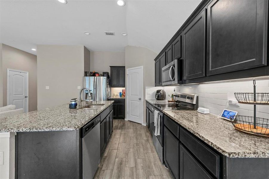 Kitchen with appliances with stainless steel finishes, an island with sink, sink, and light hardwood / wood-style floors