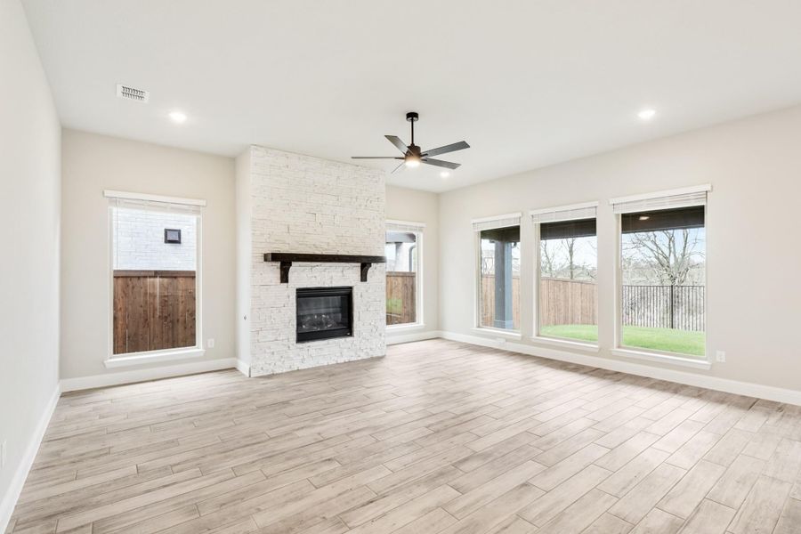 Open living room with white stone fireplace, ceiling fan, and wood-look floors