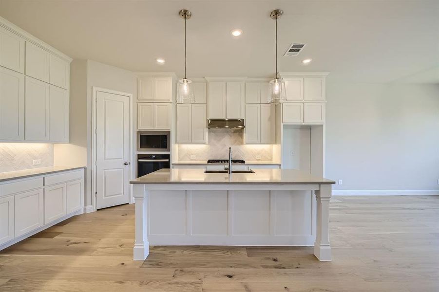 Kitchen with pendant lighting, a center island with sink, stainless steel appliances, light hardwood / wood-style floors, and decorative backsplash