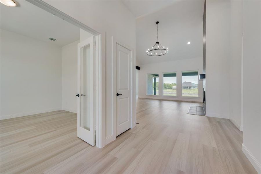 Hallway with light wood-type flooring, a notable chandelier, and a towering ceiling