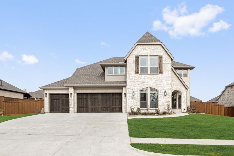 Two-story stone home with three-car garage, arched entry, and manicured front lawn