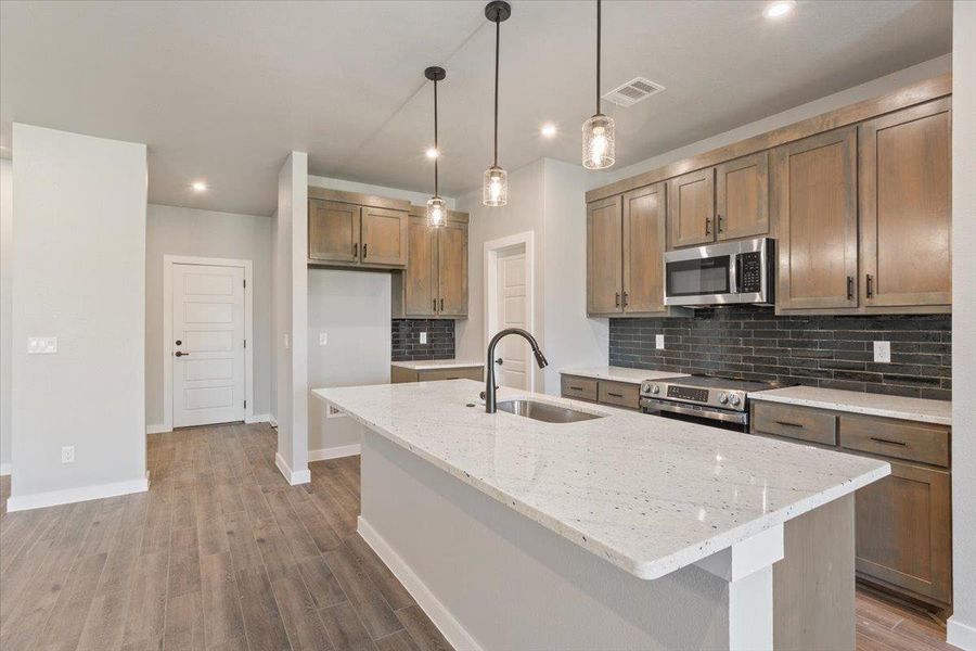 Kitchen featuring backsplash, light stone counters, decorative light fixtures, appliances with stainless steel finishes, and light wood-style floors