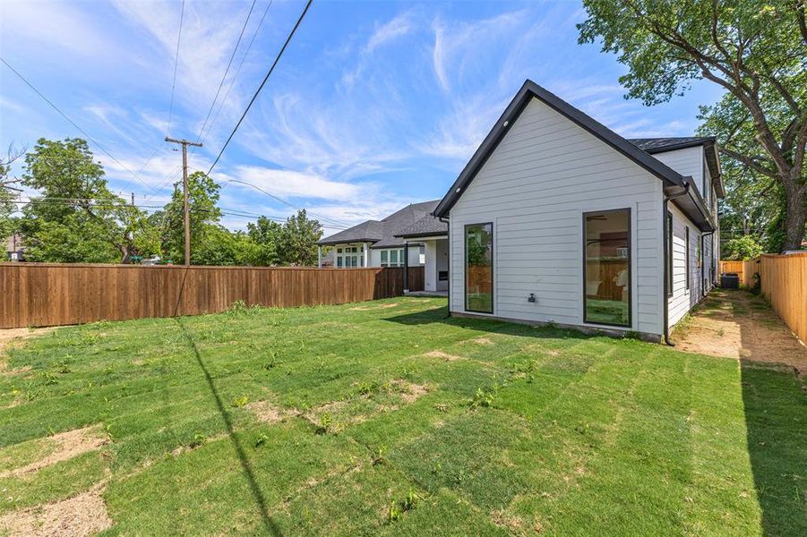 Contemporary white siding exterior with a dark-trimmed roofline, complemented by tall, black-framed windows, a private wood fence, and a green grass area