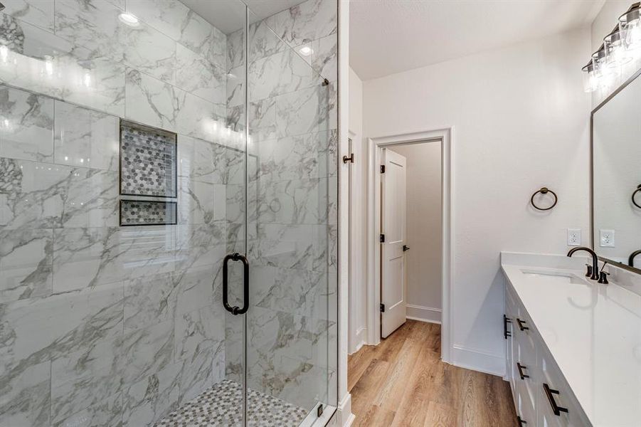 Full bath featuring baseboards, wood finished floors, vanity, and a marble finish shower Full bath featuring baseboards, wood finished floors, vanity, and a marble finish shower