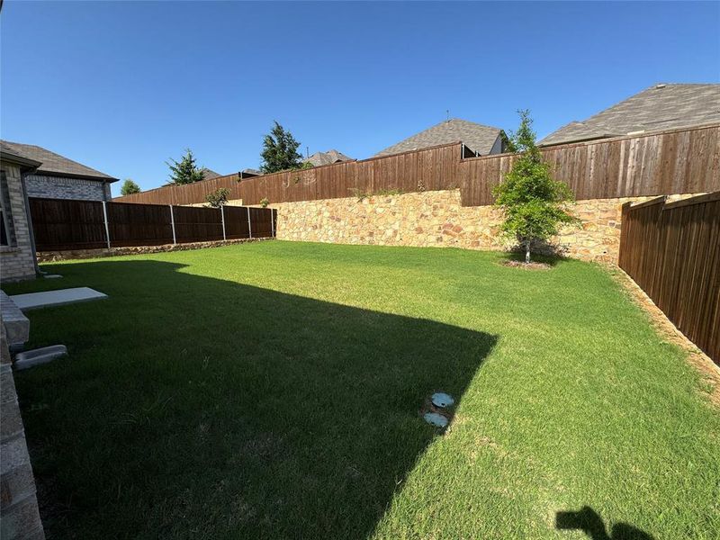 Spacious backyard featuring extensive green lawn, a stone retaining wall, and a wood privacy fence Spacious backyard featuring extensive green lawn, a stone retaining wall, and a wood privacy fence