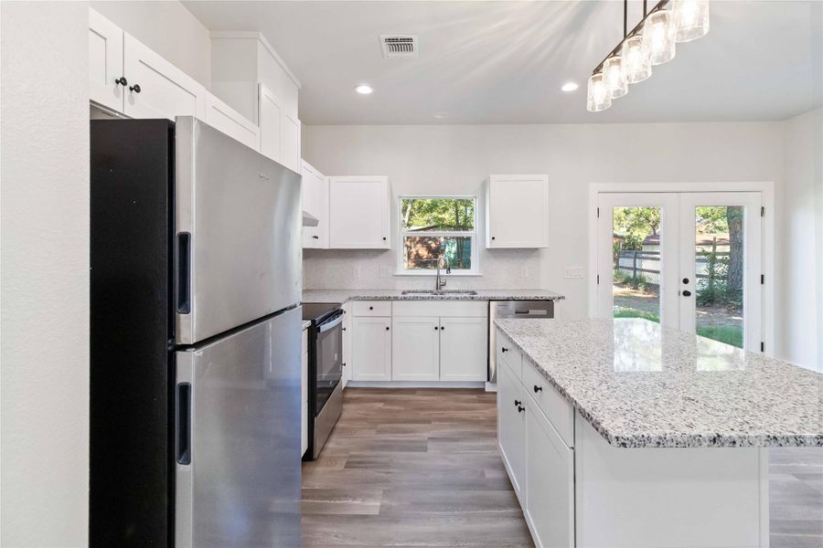 Kitchen with stainless steel appliances, white cabinets, light stone counters, french doors, and recessed lighting