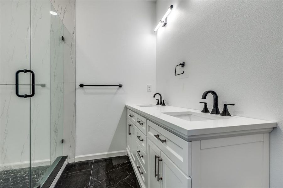 Full bath with double vanity, a marble finish shower, and dark marble finish floors Full bath with double vanity, a marble finish shower, and dark marble finish floors