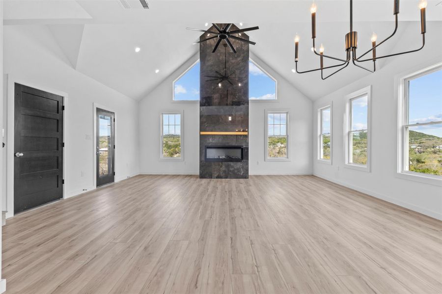 Unfurnished living room featuring a high ceiling, a fireplace, light wood-style flooring, a ceiling fan, and suspended lighting