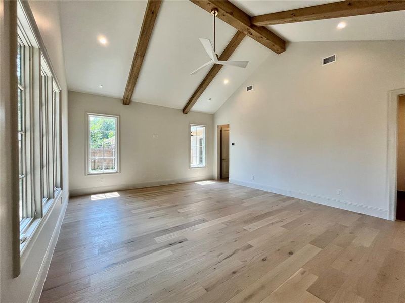 Unfurnished living room with light wood-type flooring, high vaulted ceiling, beam ceiling, and ceiling fan