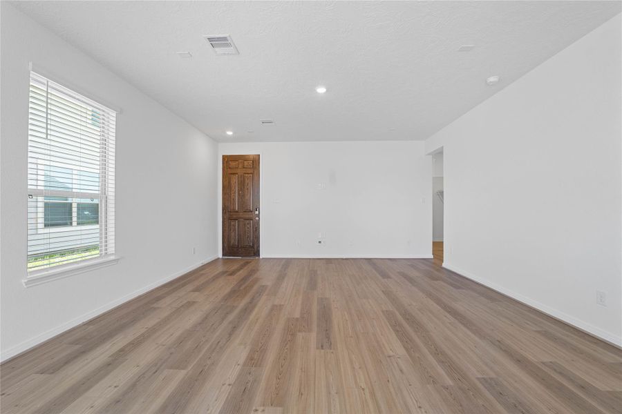 This bright and airy Great Room offers a spacious layout ideal for both relaxing evenings and lively gatherings. Designed for comfort and connection, it features vinyl plank flooring, a large window with blinds, high ceilings, recessed lighting, and seamless access to the stunning kitchen—perfect for everyday living and entertaining alike.