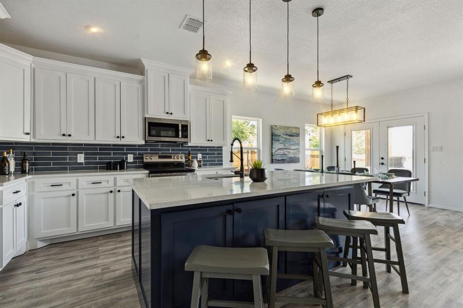 Kitchen with appliances with stainless steel finishes, a center island with sink, sink, light stone countertops, and hardwood / wood-style flooring