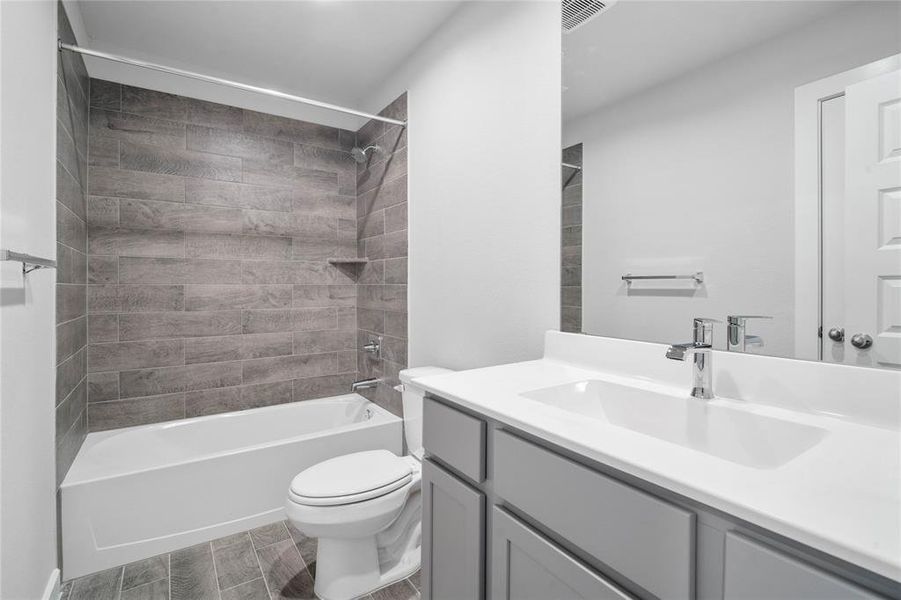 Secondary bath features tile flooring, bath/shower combo with tile surround, grey cabinets, beautiful light countertops, mirror, sleek fixtures and modern finishes.