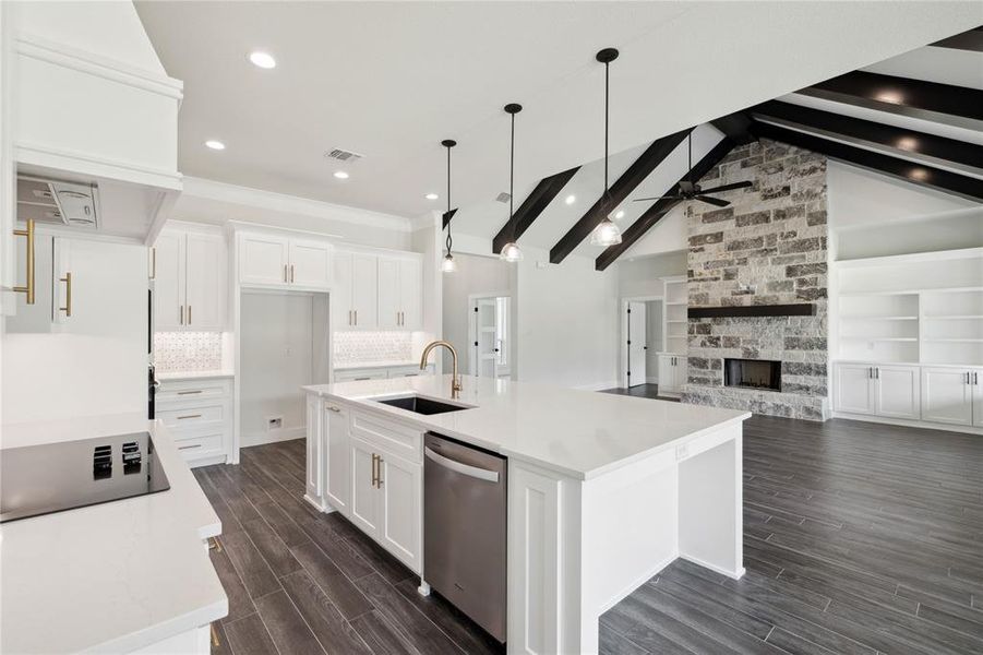 Kitchen featuring ceiling fan, dark hardwood / wood-style flooring, an island with sink, dishwasher, and a stone fireplace