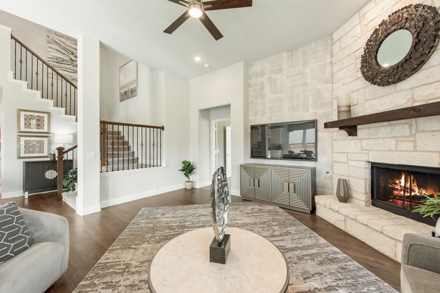 Open living room with stone fireplace, high ceilings, hardwood floors, and staircase visible in background