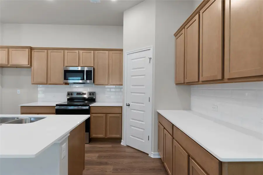 Kitchen with stainless steel appliances, dark wood-type flooring, backsplash, and light countertops