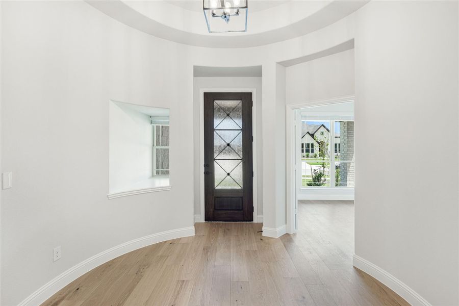Round foyer with dark wood front door, glass panels, tray ceiling, and light hardwood floors