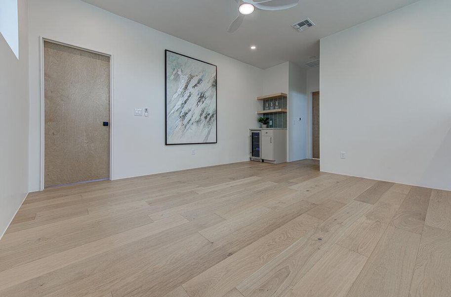 Spare room with beverage cooler, light wood finished floors, visible vents, and a ceiling fan