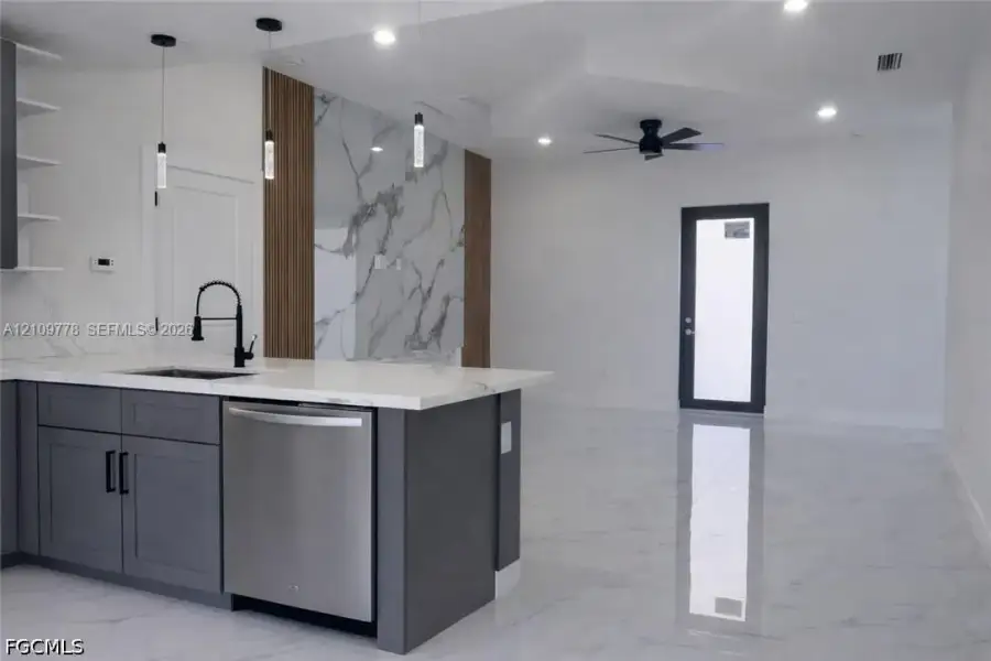 Kitchen featuring a stone-finish island countertop, matte black faucet, stainless steel dishwasher, full-height decorative wall paneling, and polished tile flooring Kitchen featuring a stone-finish island countertop, matte black faucet, stainless steel dishwasher, full-height decorative wall paneling, and polished tile flooring