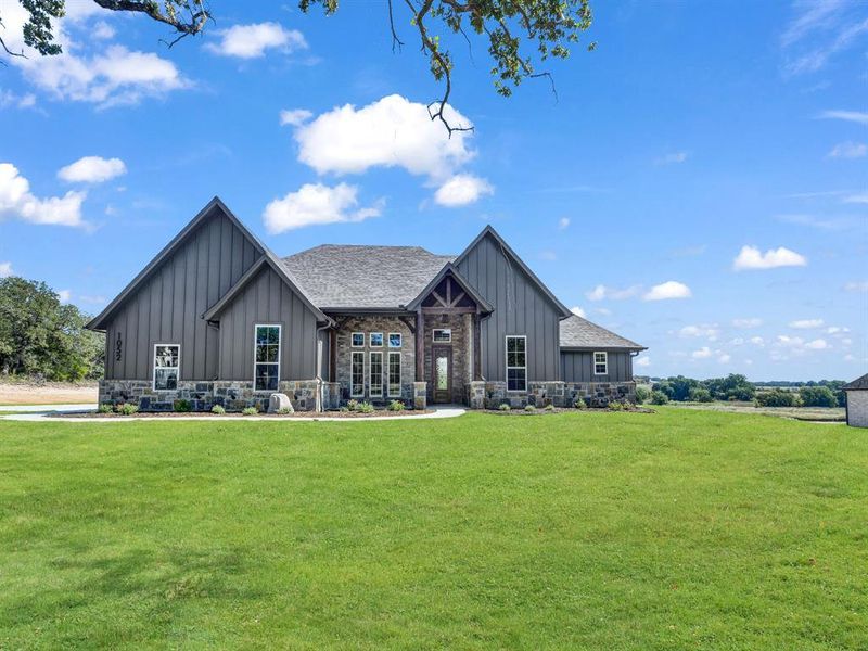 Rear view of property featuring board and batten siding, stone siding, and a yard