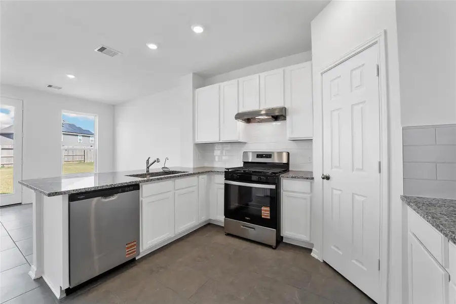 This spacious kitchen, with its high ceilings, showcases white Woodmont Belmont cabinets, complimented by granite Luna Pearl countertops and a modern Daltile backsplash. Stainless steel Whirlpool appliances, recessed lighting, and a pantry complete the space, which offers open sightlines to the expansive Great Room. This spacious kitchen, with its high ceilings, showcases white Woodmont Belmont cabinets, complimented by granite Luna Pearl countertops and a modern Daltile backsplash. Stainless steel Whirlpool appliances, recessed lighting, and a pantry complete the space, which offers open sightlines to the expansive Great Room.