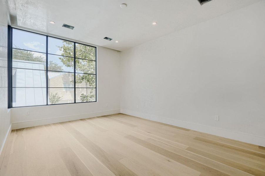 A spacious room features beautiful hardwood floors and a large multi-pane window, offering ample natural illumination.