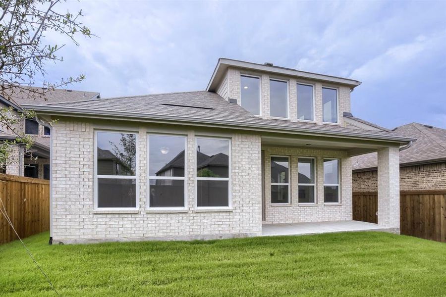 Rear exterior featuring an expansive green lawn, light-colored brick facade, covered patio, and multiple large windows