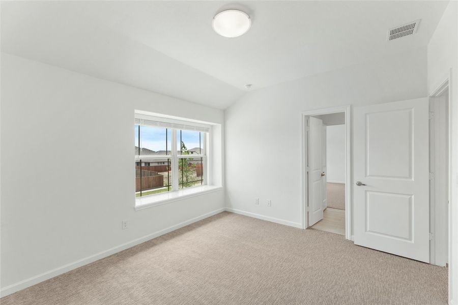 Empty bedroom with beige carpet, white walls, a large window, and two doors leading to adjoining rooms
